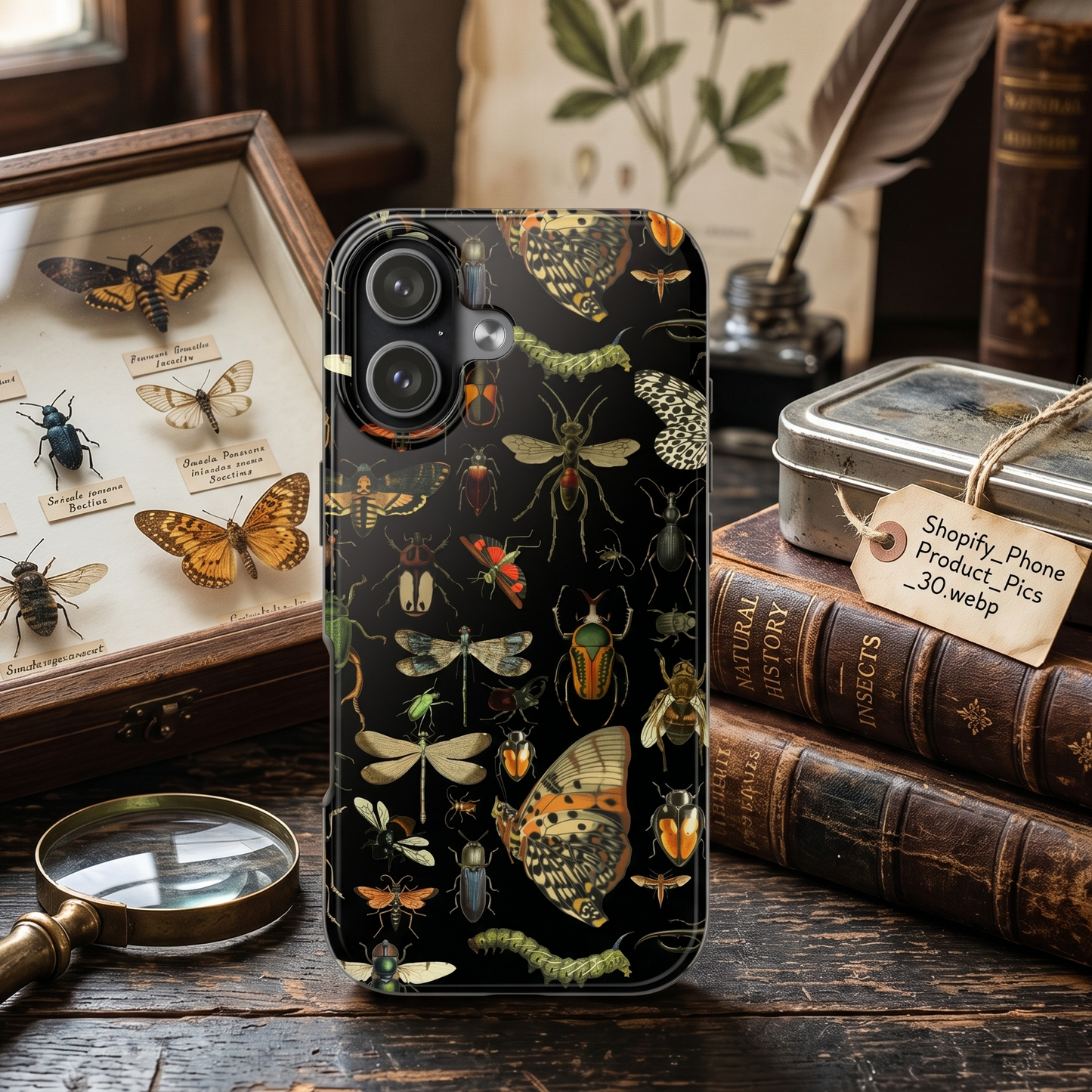 Phone case with insect design on a wooden table with books and a magnifying glass.