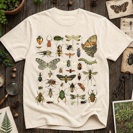 An off-white short-sleeve t-shirt with a detailed graphic print of various vintage-style insects, butterflies, and caterpillars, laid flat on a rustic dark wood background surrounded by botanical props.